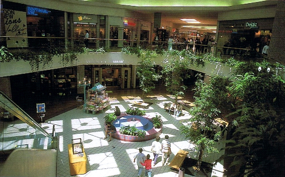 Historic interior view of Vallco Fashion Park in Cupertino circa 1990 showing two levels of shops, skylights, plants, and shoppers inside the mall