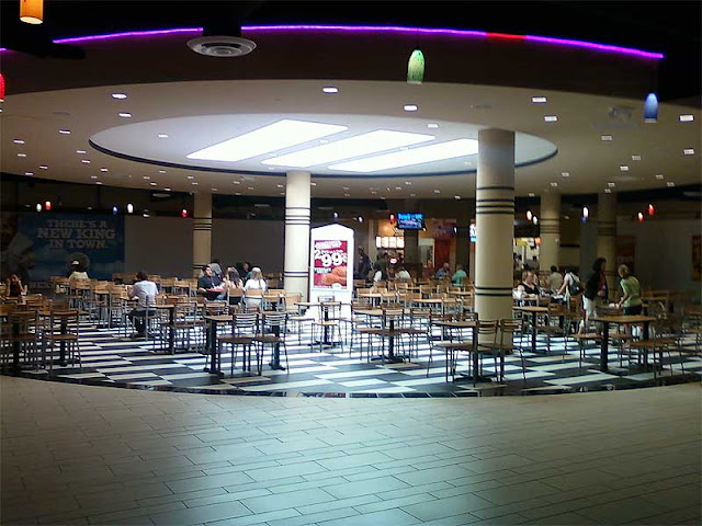 Vallco Mall food court in Cupertino in 2009 with tables, chairs, neon lighting, columns, and casual dining areas