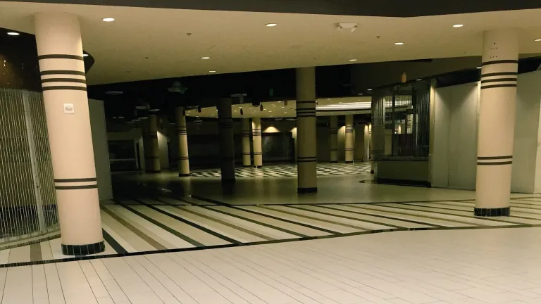 Empty interior corridor of Vallco Mall in Cupertino with tile floors, columns, closed storefronts, and dim lighting