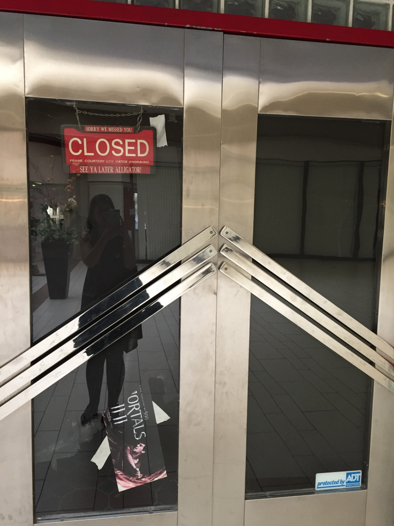 Closed storefront inside Vallco Mall in Cupertino with a red closed sign and empty retail space behind glass doors